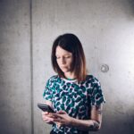 Ines liest Newsletter auf ihrem Handy vor einer grauen Wand
